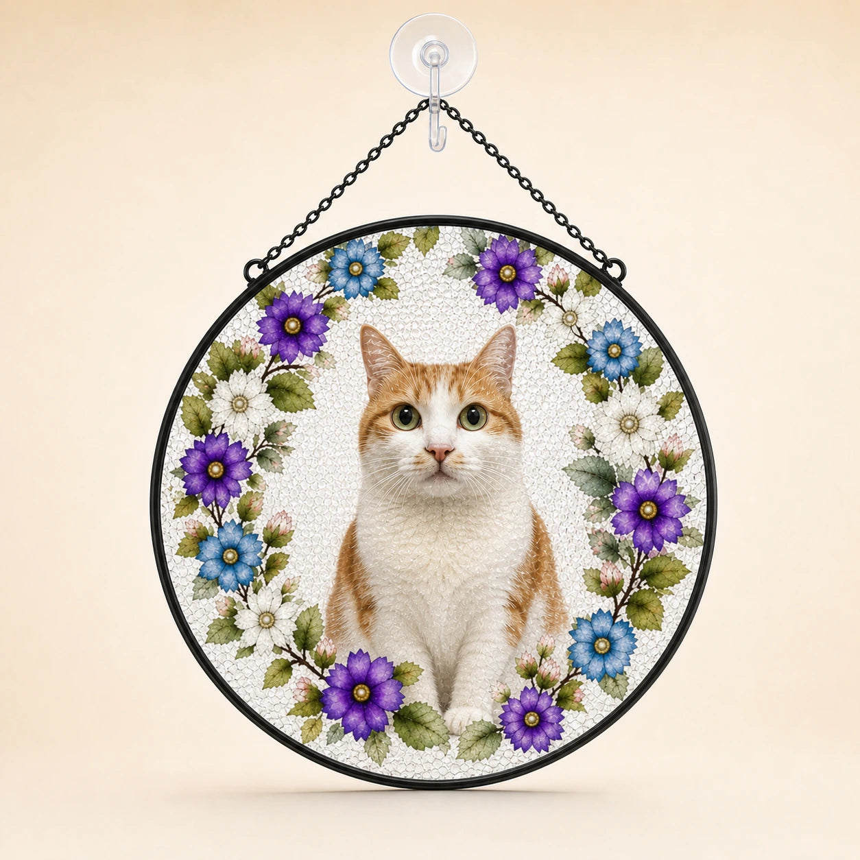 Round hanging decorative sign featuring a white and orange cat centered within a floral wreath of purple, blue, and white flowers, suspended by a black chain from a clear wall hook against a warm beige background.