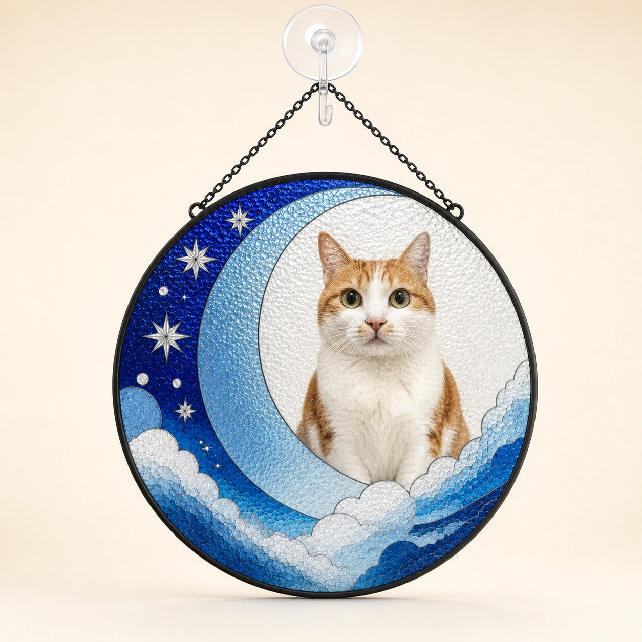 A circular hanging decorative sign featuring a photo of an orange and white cat seated on a crescent moon with stars and clouds, suspended by a black chain from a clear wall hook against a warm beige background.