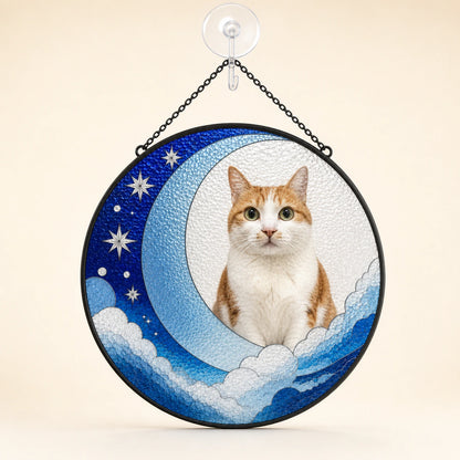 A circular hanging decorative sign featuring a photo of an orange and white cat seated on a crescent moon with stars and clouds, suspended by a black chain from a clear wall hook against a warm beige background.